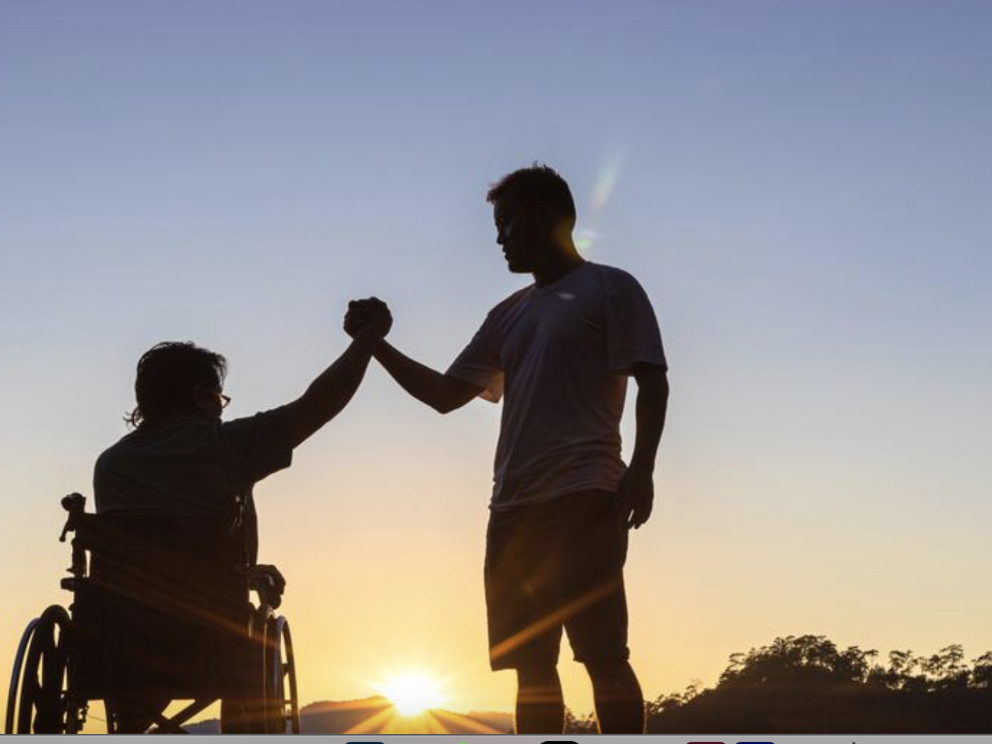 Una persona in carrozzina ed un ragazzo in piedi si stringono il pugno sullo sfondo di un paesaggio naturale al tramonto.
