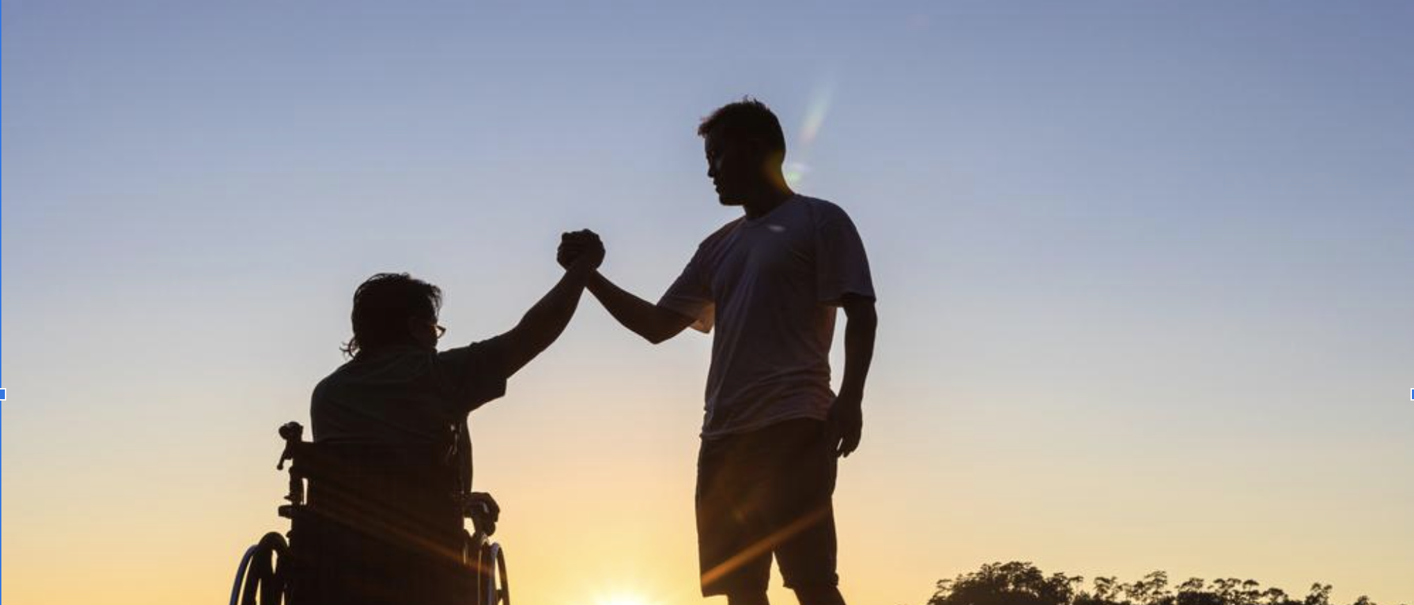 Una persona in carrozzina ed un ragazzo in piedi si stringono il pugno sullo sfondo di un paesaggio naturale al tramonto.